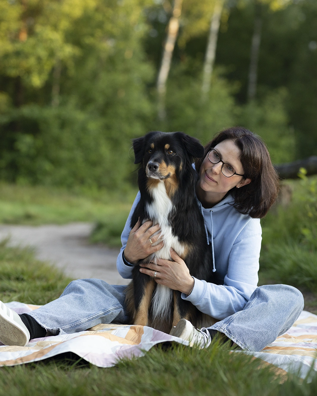 Frau umarmt ihren Hund auf einer Decke im Freien.