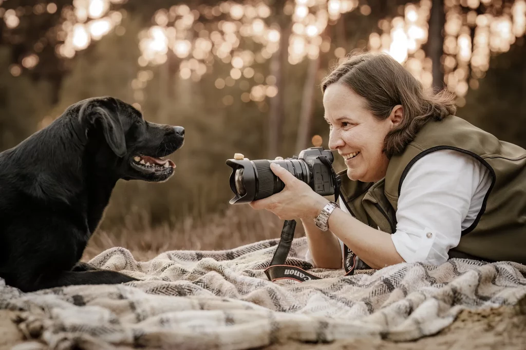 Frau fotografiert einen schwarzen Labrador im Freien.